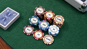 MRC Poker Monte Carlo poker chips in various denominations stacked on a green felt table next to a deck of cards