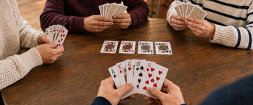 Four players enjoying a game of Euchre around a wooden table with gold-backed playing cards.